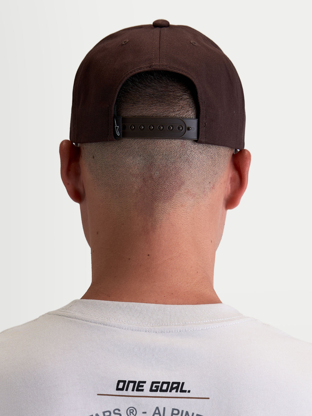 Alpinestars Combo Logo Snapback pet, casual motorsport sportswear-pet voor heren en dames, bruin, duurzame keperstof, achteraanzicht op model met verstelbare snapbacksluiting en merklabel.