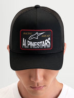 Alpinestars Hemmings Trucker Pet, zwarte sportswear snapback pet gedragen door een model, met een geweven logopatch op de voorkant en ademende mesh achterpanelen