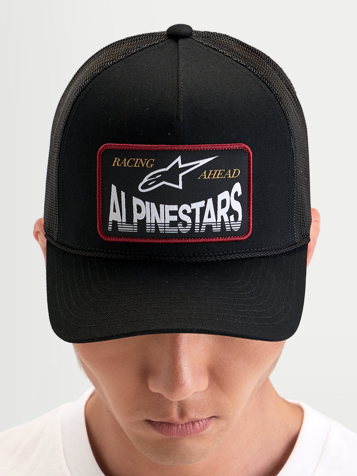 Alpinestars Hemmings Trucker Pet, zwarte sportswear snapback pet gedragen door een model, met een geweven logopatch op de voorkant en ademende mesh achterpanelen