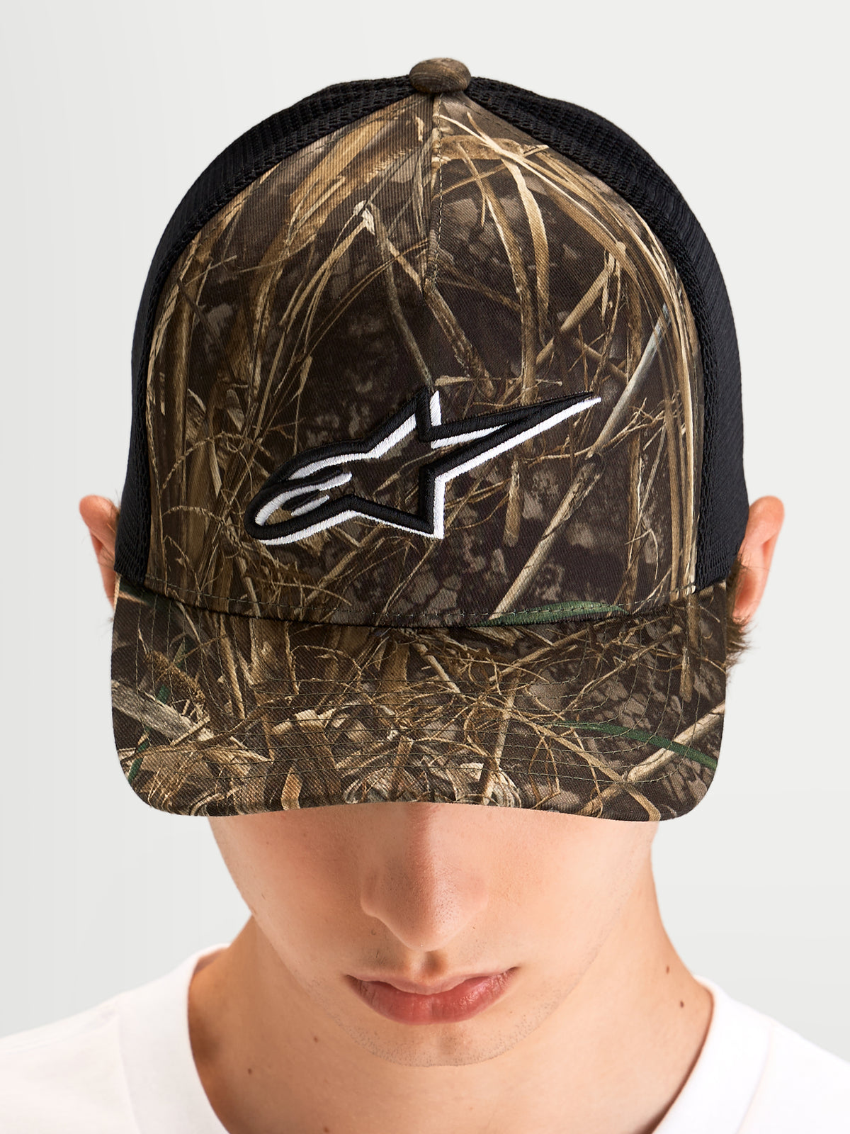 Alpinestars Thicket Realtree Trucker pet, sportswear trucker pet gedragen door een model, Realtree-camouflage en zwart, gebogen klep, gestructureerd kroon en wit geborduurd Astars-logo op de voorkant