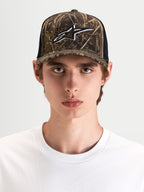Alpinestars Thicket Realtree Trucker pet, sportswear snapback pet in camouflage en zwart, gedragen door model met gestructureerde kroon en geborduurd Astars-logo op het voorpaneel