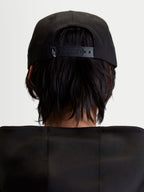 Alpinestars Label Snapback pet, zwarte sportswearpet voor heren en dames, achteraanzicht op model met verstelbare snapbacksluiting en klein wit logo, constructie van katoenen keperstof
