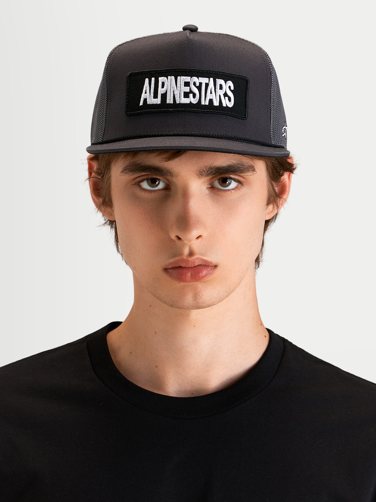 Alpinestars Ten Trucker pet, donkergrijze sportswear cap met platte klep en gestructureerde kroon, gedragen door een model, voorzien van een geborduurde Alpinestars woordlogopatch op de voorzijde