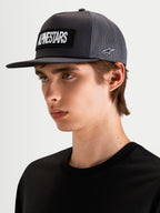 Alpinestars Ten Trucker pet, lifestyle pet met platte klep in donkergrijs, gedragen door model, met geborduurd Alpinestars woordlogo op de voorkant en Astars-logo op de zijkant