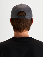 Alpinestars Ten Trucker pet, sportieve snapback pet in donkergrijs, achteraanzicht op model met verstelbare snapbacksluiting, mesh rugpanelen en achteretikettering