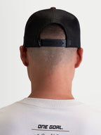 Alpinestars Hotlink Trucker pet, sportswear lifestyle pet, unisex, bruin en zwart, achteraanzicht op model met verstelbare snapback-sluiting, mesh panelen voor ademend vermogen en premium merkdetails.
