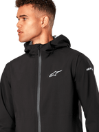 Alpinestars Kascade regenjas, zwarte shell regenjas, met een wit sterlogo op de borst, vaste capuchon en gecoate omgekeerde spiraalrits aan de voorkant, casual op motorsport geïnspireerde performance-bovenkleding