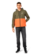Alpinestars Speeder Windbreaker jas, kleurblokken in Military Green en oranje, lichtgewicht jas met capuchon, zwarte trekkoorden en ritssluiting, wit logo op de borst en mouw, gedragen met donkere jeans en zwarte sneakers, casual sportswear stijl.