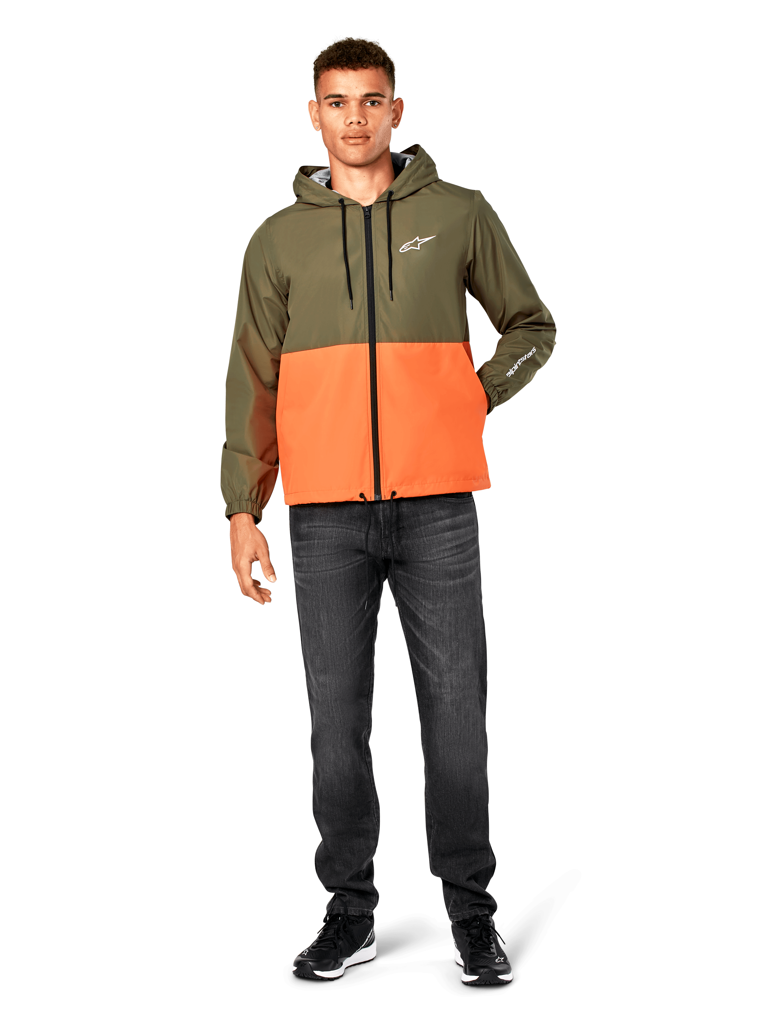 Alpinestars Speeder Windbreaker jas, kleurblokken in Military Green en oranje, lichtgewicht jas met capuchon, zwarte trekkoorden en ritssluiting, wit logo op de borst en mouw, gedragen met donkere jeans en zwarte sneakers, casual sportswear stijl.