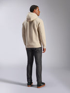 Alpinestars Ageless V3 Hoodie, casual off-white fleece trui met capuchon van de achterkant gezien, voorzien van geribde manchetten en zoom, gedragen met een donkere slim-fit jeans en zwarte Alpinestars sneakers