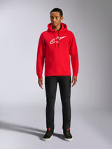 Alpinestars Ageless V3 Hoodie, casual streetwear, rood met wit geborduurd Alpinestars-logo, gedragen door een mannelijk model met zwarte broek, capuchon met trekkoord, kangoeroezak aan de voorzijde, modern op de motorsport geïnspireerd ontwerp