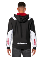 Alpinestars Sessions V3 Hoodie, achteraanzicht, zwart met witte mouwpanelen en rode capuchonvoering, voorzien van wit woordmerk op de rug en rode branding op de mouwen, casual streetwear geïnspireerd op de motorsport