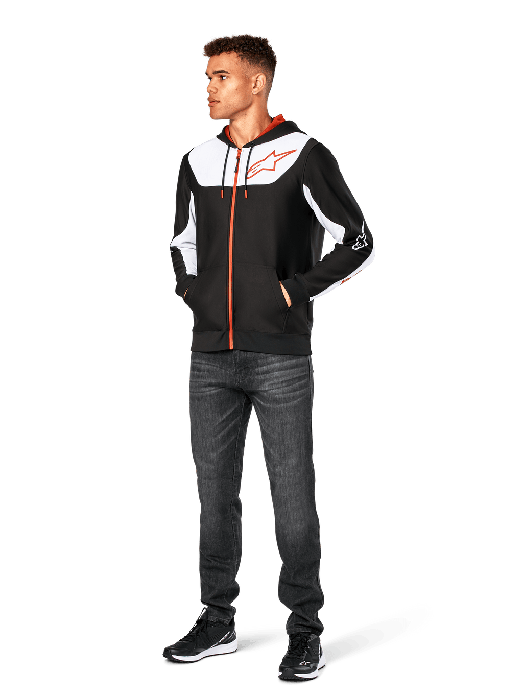 Alpinestars Sessions V3 Hoodie, casual hoodie met ritssluiting, zwart, wit en rood, gedragen door model met donkere jeans en zwarte sneakers, voorzien van witte kleurvlakken op de borst en mouwen, rode rits- en trekkoorddetails, groot logo op de borst, poly-fleece motorsport-geïnspireerde streetwear