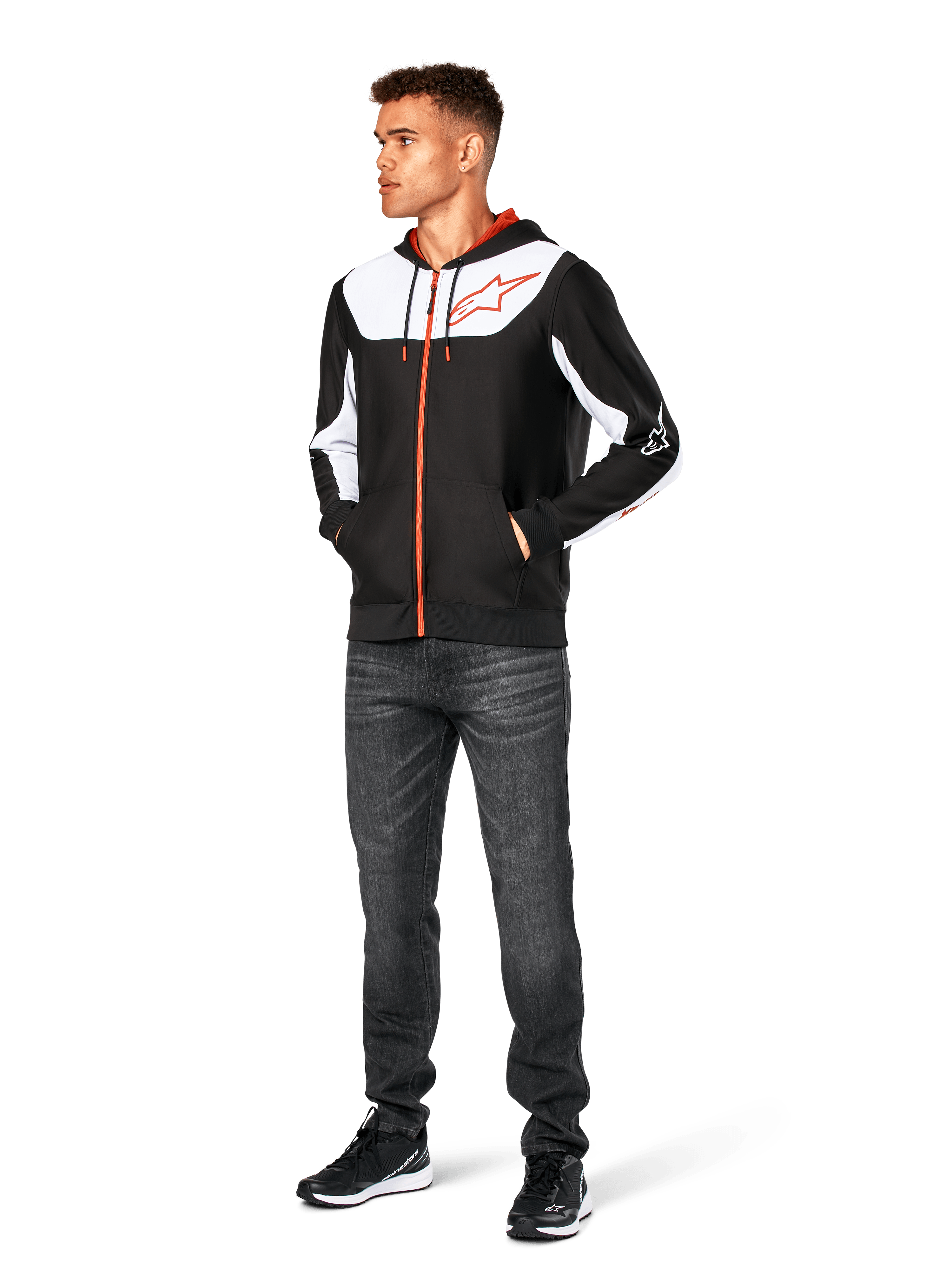 Alpinestars Sessions V3 Hoodie, casual hoodie met ritssluiting, zwart, wit en rood, gedragen door model met donkere jeans en zwarte sneakers, voorzien van witte kleurvlakken op de borst en mouwen, rode rits- en trekkoorddetails, groot logo op de borst, poly-fleece motorsport-geïnspireerde streetwear