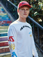 Alpinestars Profile pet, rood, gedragen door een jongeman, gestructureerde kroon met gebogen klep en geborduurd logo, gecombineerd met een wit graphic T-shirt met lange mouwen, casual motorsport streetwear