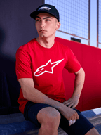 Alpinestars Profile pet in het zwart, lifestyle-opname van een man die de pet met gebogen klep draagt, gecombineerd met een rood t-shirt met een wit Alpinestars-logo, casual op motorsport geïnspireerde streetwear