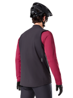 Alpinestars A-Dura Thermovest, zwart, achteraanzicht, gedragen over een bordeauxrode jersey met lange mouwen, met een zwarte mountainbikehelm en handschoenen, lichtgewicht geïsoleerde fietskleding voor off-road rijden