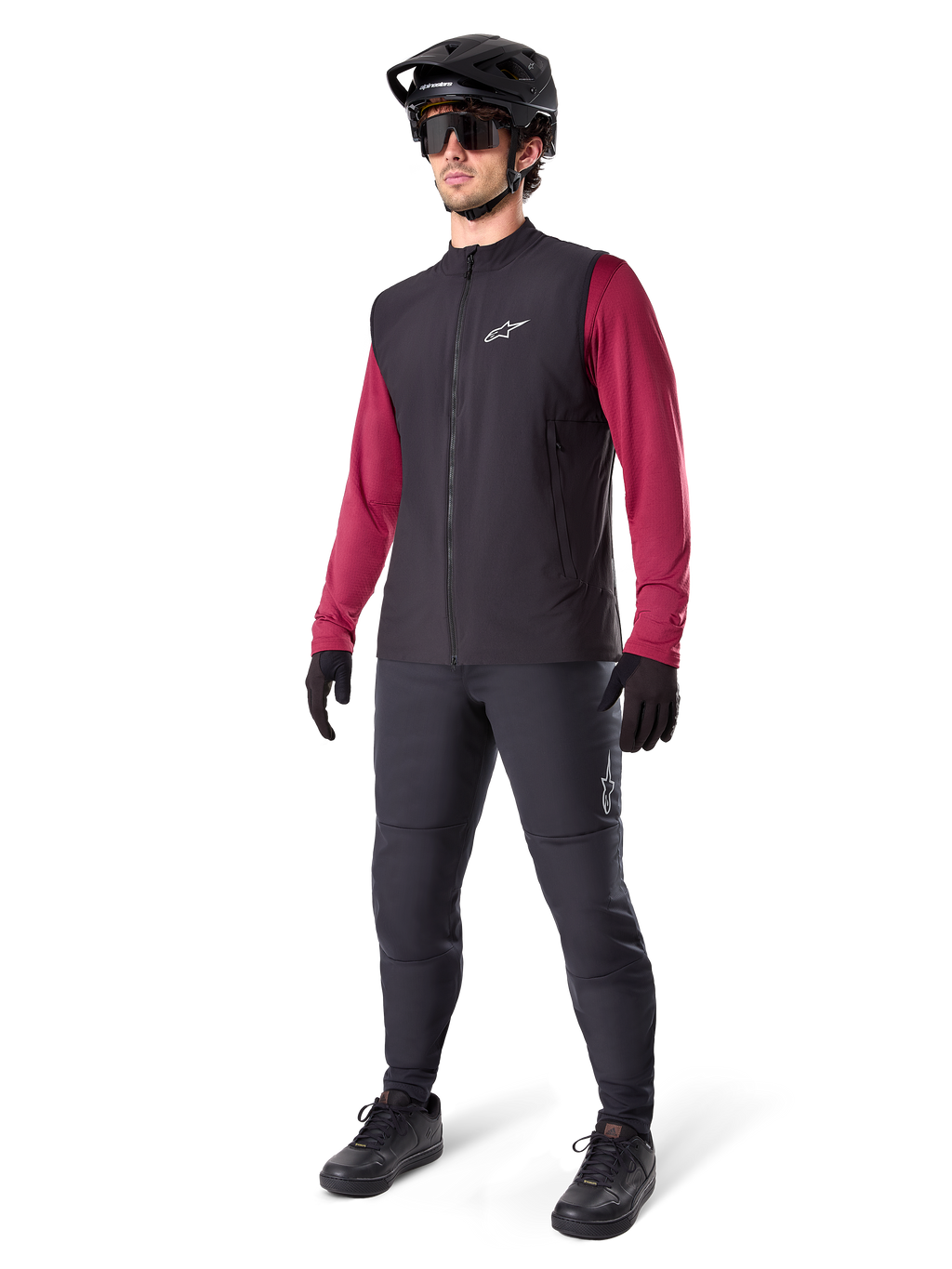 Alpinestars A-Dura Thermal Vest, zwart fietsvest, gedragen door een rijder over een bordeauxrode jersey met lange mouwen en een zwarte broek, inclusief zwarte MTB-helm en handschoenen, ontworpen voor mountainbiken in koud weer