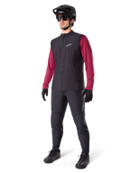 Alpinestars A-Dura Thermal Vest, zwart fietsvest, gedragen door een rijder over een bordeauxrode jersey met lange mouwen en een zwarte broek, inclusief zwarte MTB-helm en handschoenen, ontworpen voor mountainbiken in koud weer
