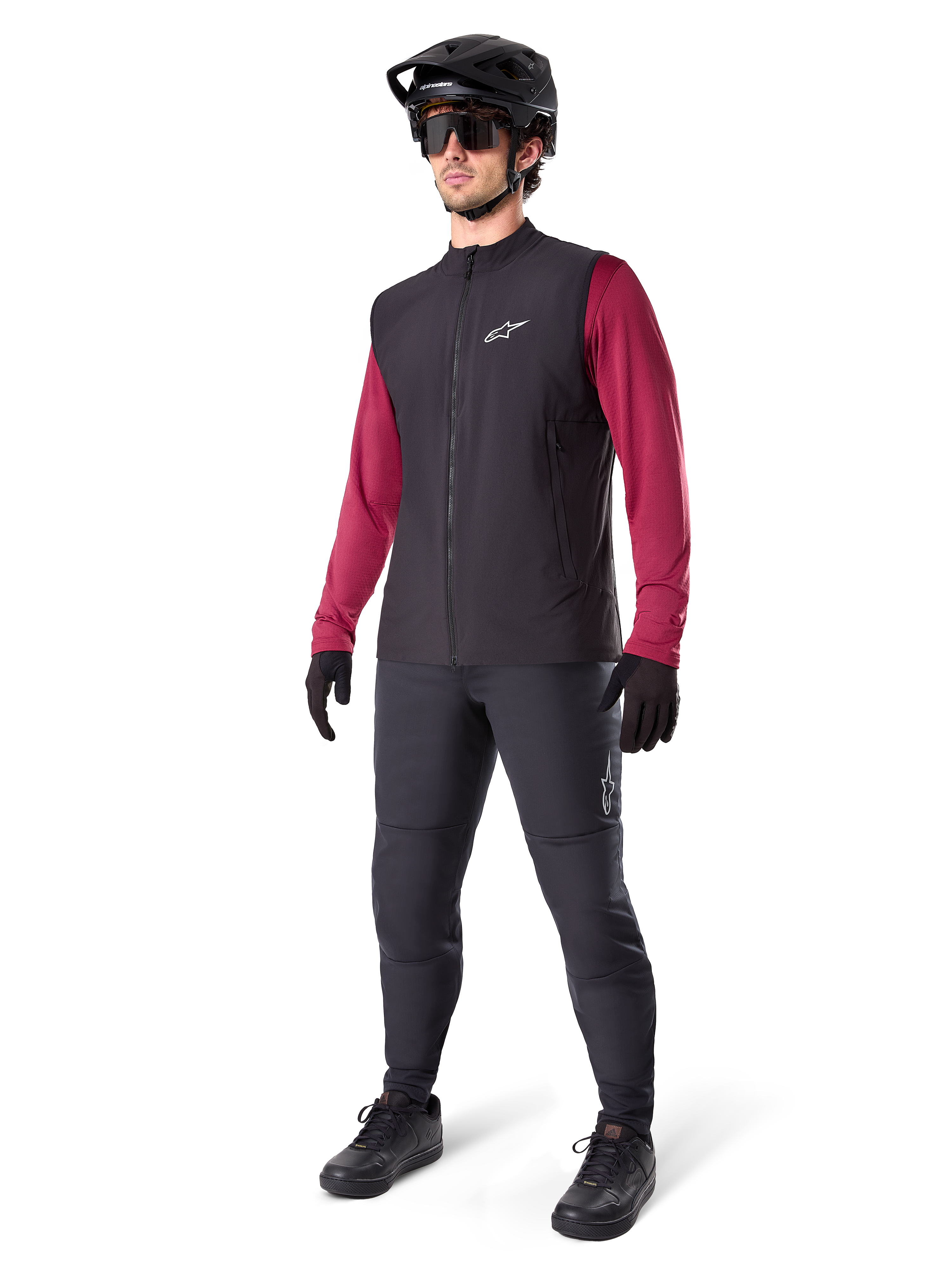 Alpinestars A-Dura Thermal Vest, zwart fietsvest, gedragen door een rijder over een bordeauxrode jersey met lange mouwen en een zwarte broek, inclusief zwarte MTB-helm en handschoenen, ontworpen voor mountainbiken in koud weer