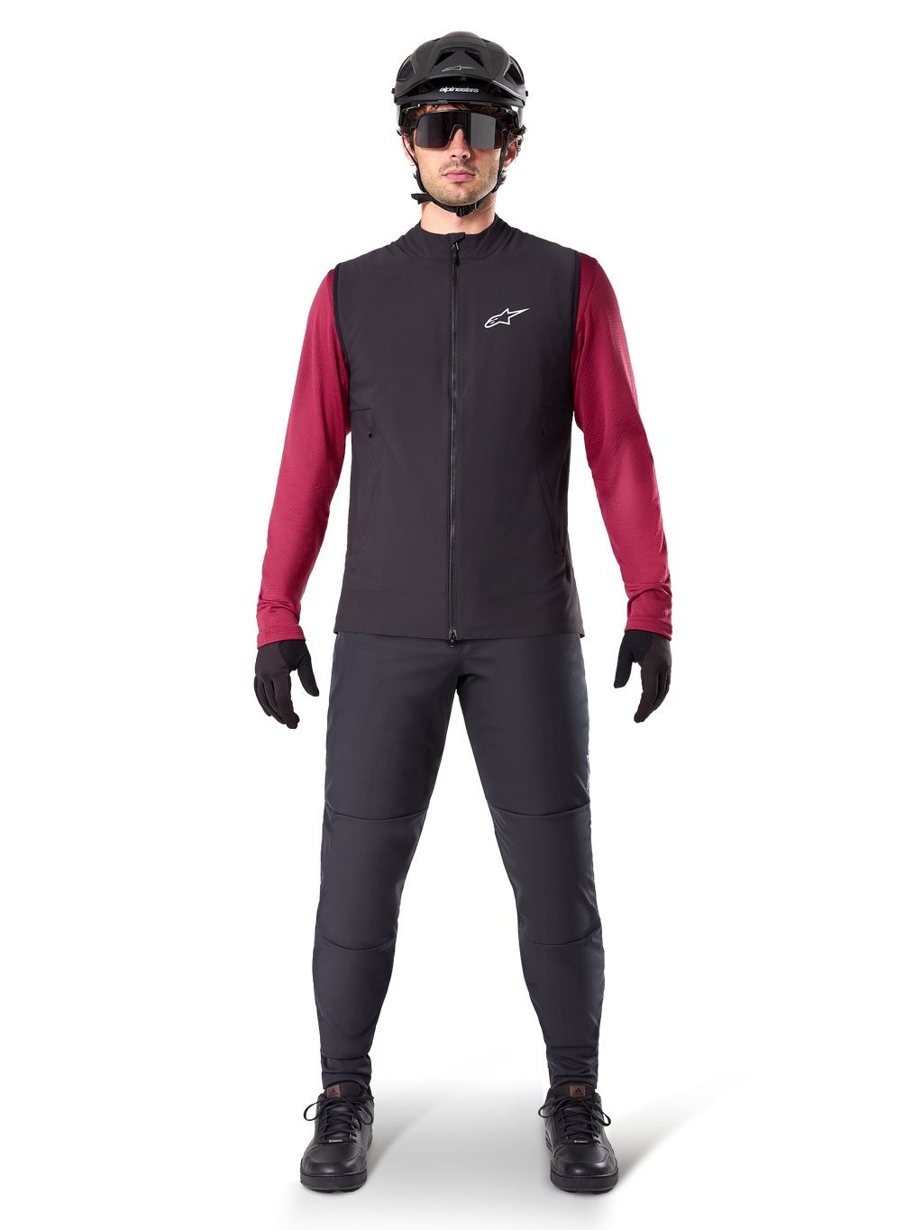 Alpinestars A-Dura Thermal Vest, zwart fietsvest gedragen over een bordeauxrode jersey met lange mouwen, gecombineerd met een donkergrijze MTB-broek, zwarte helm en zonnebril, technische mountainbikekleding voor ritten in koud weer