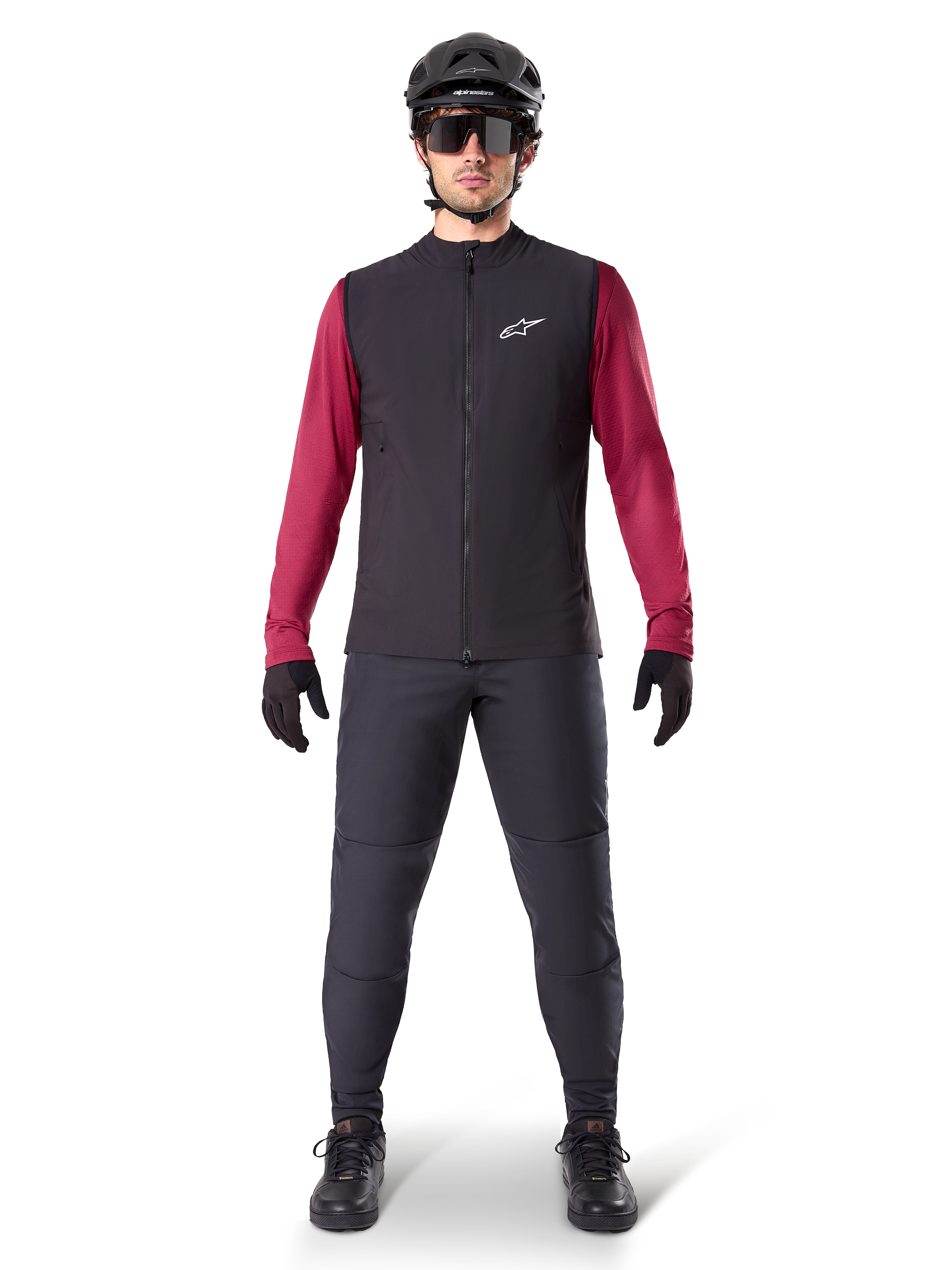 Alpinestars A-Dura Thermal Vest, zwart fietsvest gedragen over een bordeauxrode jersey met lange mouwen, gecombineerd met een donkergrijze MTB-broek, zwarte helm en zonnebril, technische mountainbikekleding voor ritten in koud weer