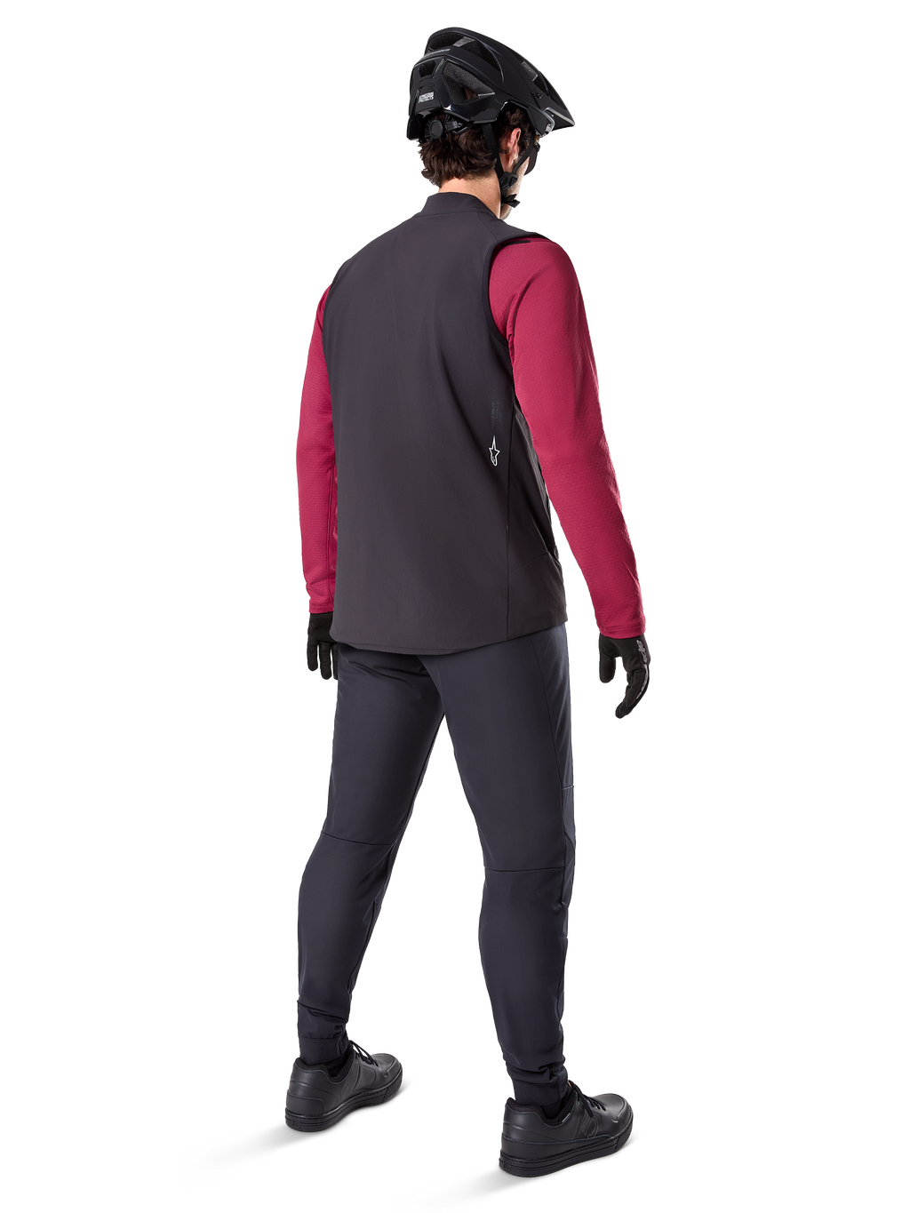 Alpinestars A-Dura Thermal Vest, zwart fietsvest, achteraanzicht op een model met een bordeauxrode jersey met lange mouwen en een zwarte fietsbroek, gecombineerd met een zwarte mountainbikehelm en handschoenen, technische uitrusting voor ritten in koud weer