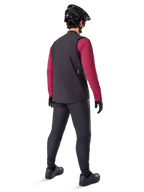 Alpinestars A-Dura Thermal Vest, zwart fietsvest, achteraanzicht op een model met een bordeauxrode jersey met lange mouwen en een zwarte fietsbroek, gecombineerd met een zwarte mountainbikehelm en handschoenen, technische uitrusting voor ritten in koud weer