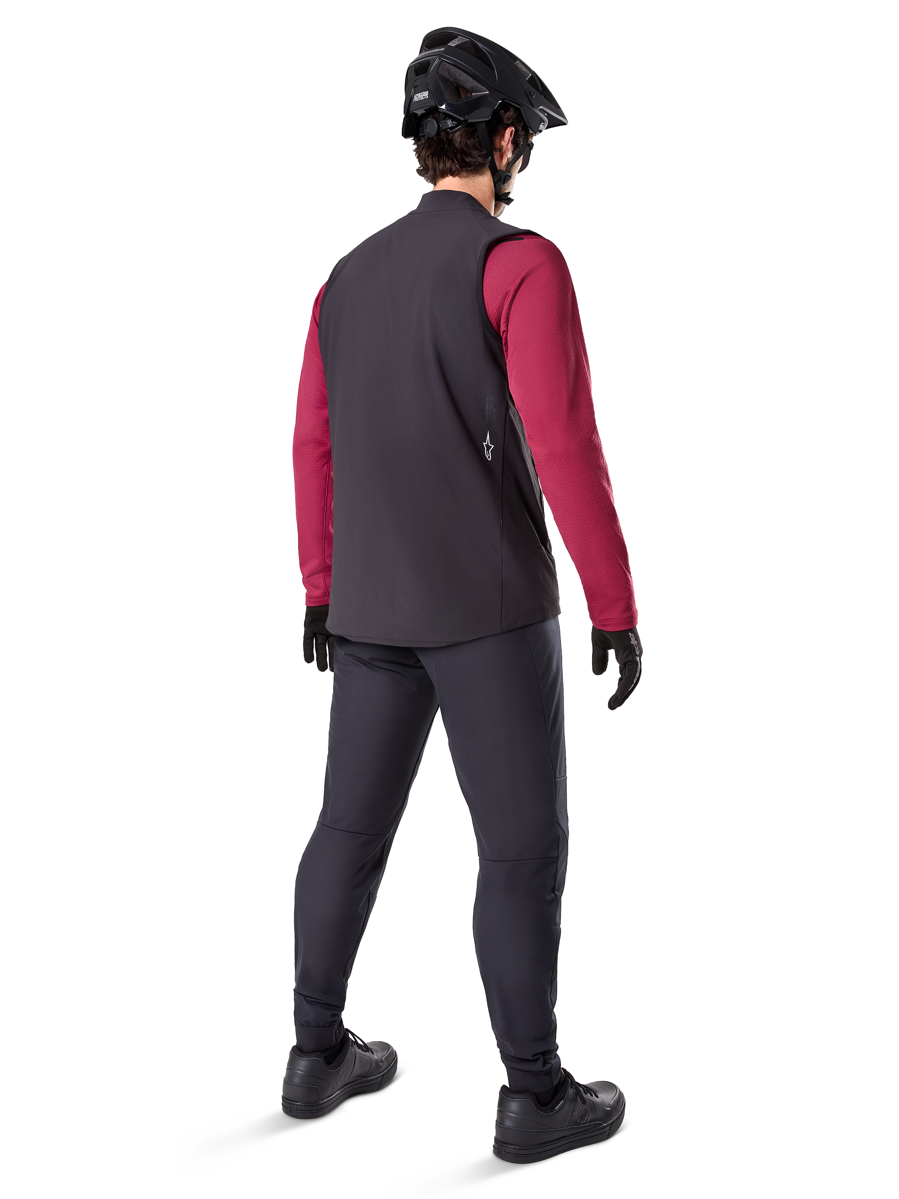 Alpinestars A-Dura Thermal Vest, zwart fietsvest, achteraanzicht op een model met een bordeauxrode jersey met lange mouwen en een zwarte fietsbroek, gecombineerd met een zwarte mountainbikehelm en handschoenen, technische uitrusting voor ritten in koud weer