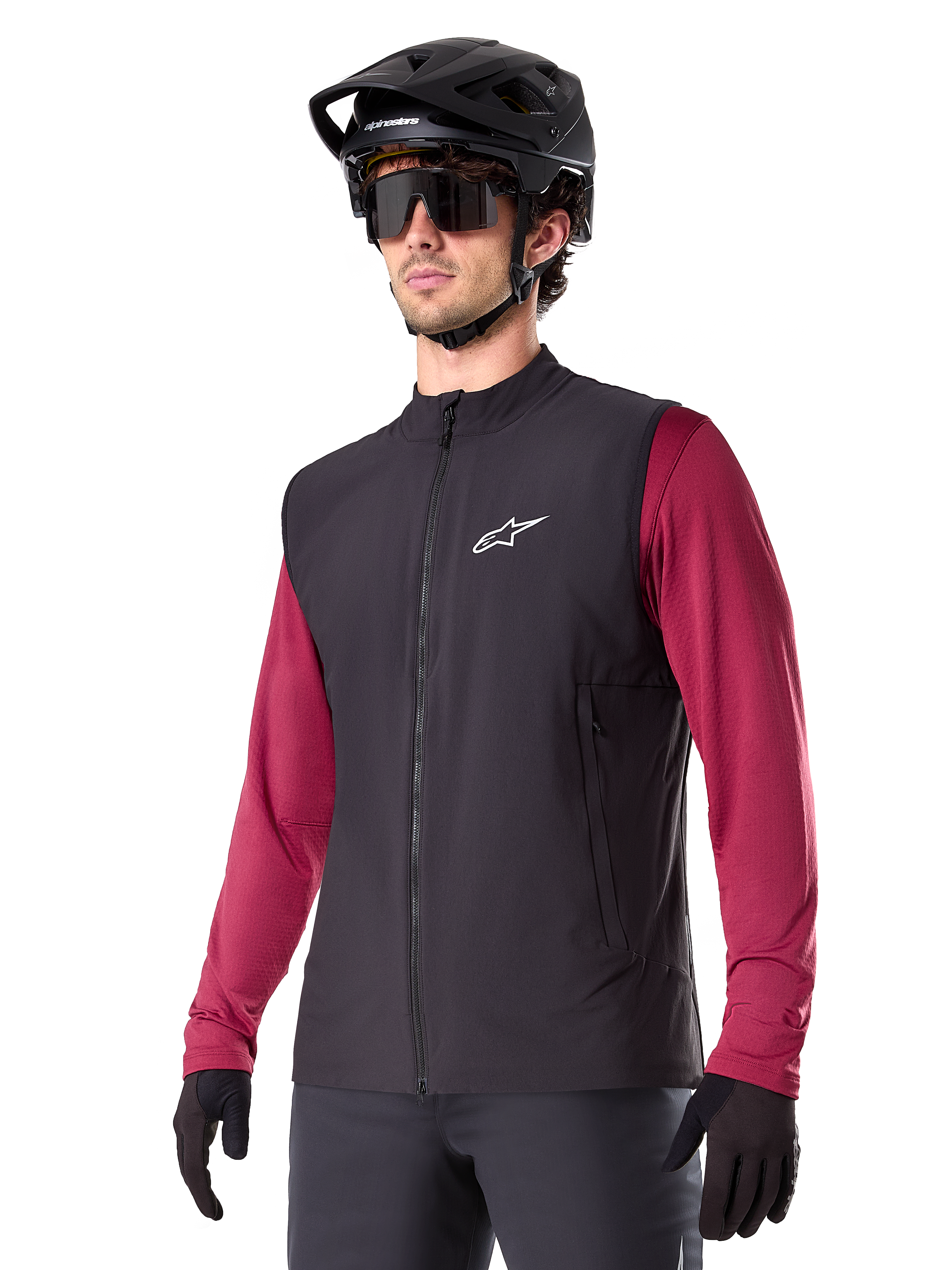 Alpinestars A-Dura Thermal Vest, zwart thermisch fietsvest, gedragen over een bordeauxrood shirt met lange mouwen, voorzien van een wit logo op de borst, gecombineerd met een zwarte MTB-helm en zonnebril, geïsoleerde prestatielaag voor mountainbiken