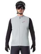 Alpinestars A-Dura Thermal Vest, fietsbodywarmer, Titanium grijs, gedragen met een zwarte jersey met lange mouwen en zwarte fietshelm, rood Alpinestars ster-logo op de borst, lichtgewicht en geïsoleerd voor mountainbiken.