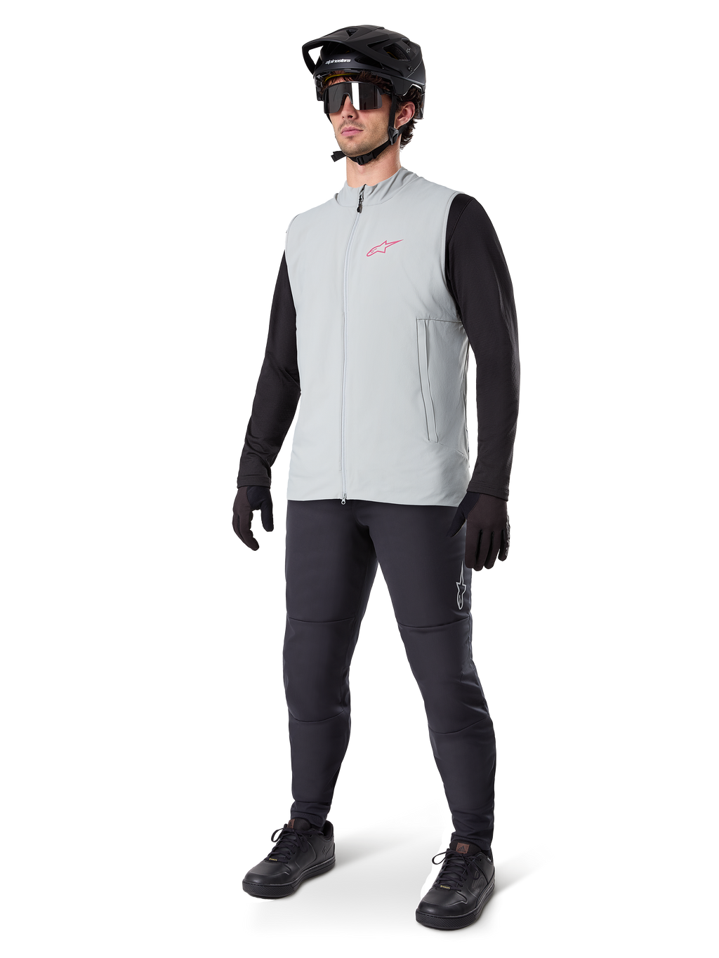 Alpinestars A-Dura Thermal Vest, titanium grijs fietsvest met een roze logo, gedragen door een model met een zwart shirt met lange mouwen, donkergrijze broek en een zwarte mountainbikehelm, performance kleding voor ritten in koud weer