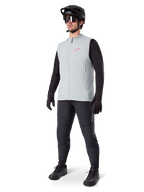 Alpinestars A-Dura Thermal Vest, titanium grijs fietsvest met een roze logo, gedragen door een model met een zwart shirt met lange mouwen, donkergrijze broek en een zwarte mountainbikehelm, performance kleding voor ritten in koud weer