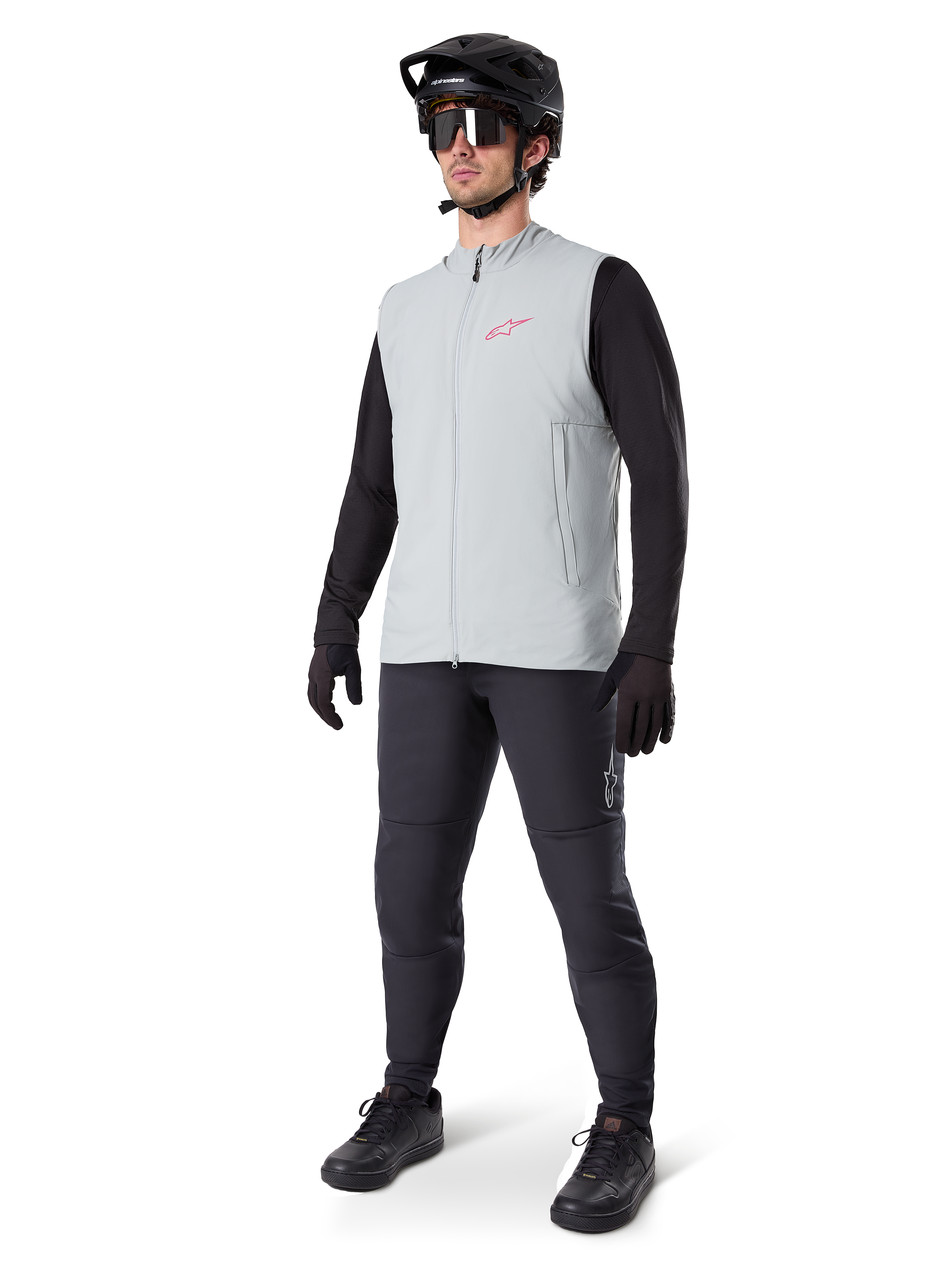 Alpinestars A-Dura Thermal Vest, titanium grijs fietsvest met een roze logo, gedragen door een model met een zwart shirt met lange mouwen, donkergrijze broek en een zwarte mountainbikehelm, performance kleding voor ritten in koud weer