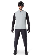 Alpinestars A-Dura Thermal Vest, fietsvest, Titanium grijs, gedragen met zwarte jersey met lange mouwen en zwarte broek, zwarte helm en zonnebril, voorzien van een rood Alpinestars-logo, lichtgewicht thermische isolatie voor mountainbiken