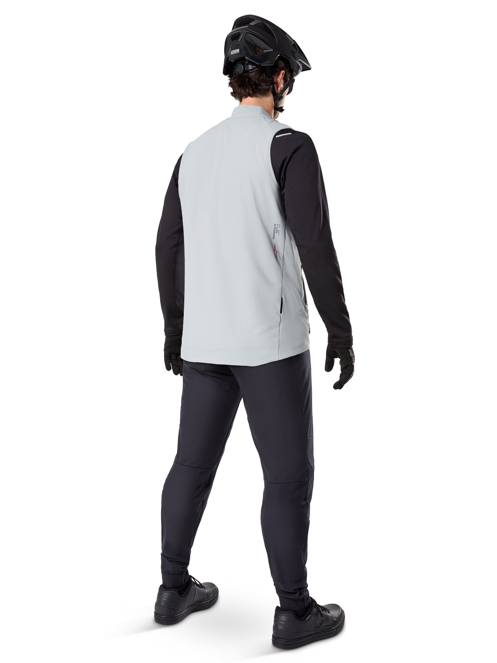 Alpinestars A-Dura Thermovest, Titanium Gray, achteraanzicht van een model dat het geïsoleerde fietsvest draagt over een zwart shirt met lange mouwen en een donkere broek, compleet met zwarte mountainbikehelm en handschoenen, ontworpen voor off-road ritten in koud weer