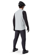 Alpinestars A-Dura Thermovest, Titanium Gray, achteraanzicht van een model dat het geïsoleerde fietsvest draagt over een zwart shirt met lange mouwen en een donkere broek, compleet met zwarte mountainbikehelm en handschoenen, ontworpen voor off-road ritten in koud weer
