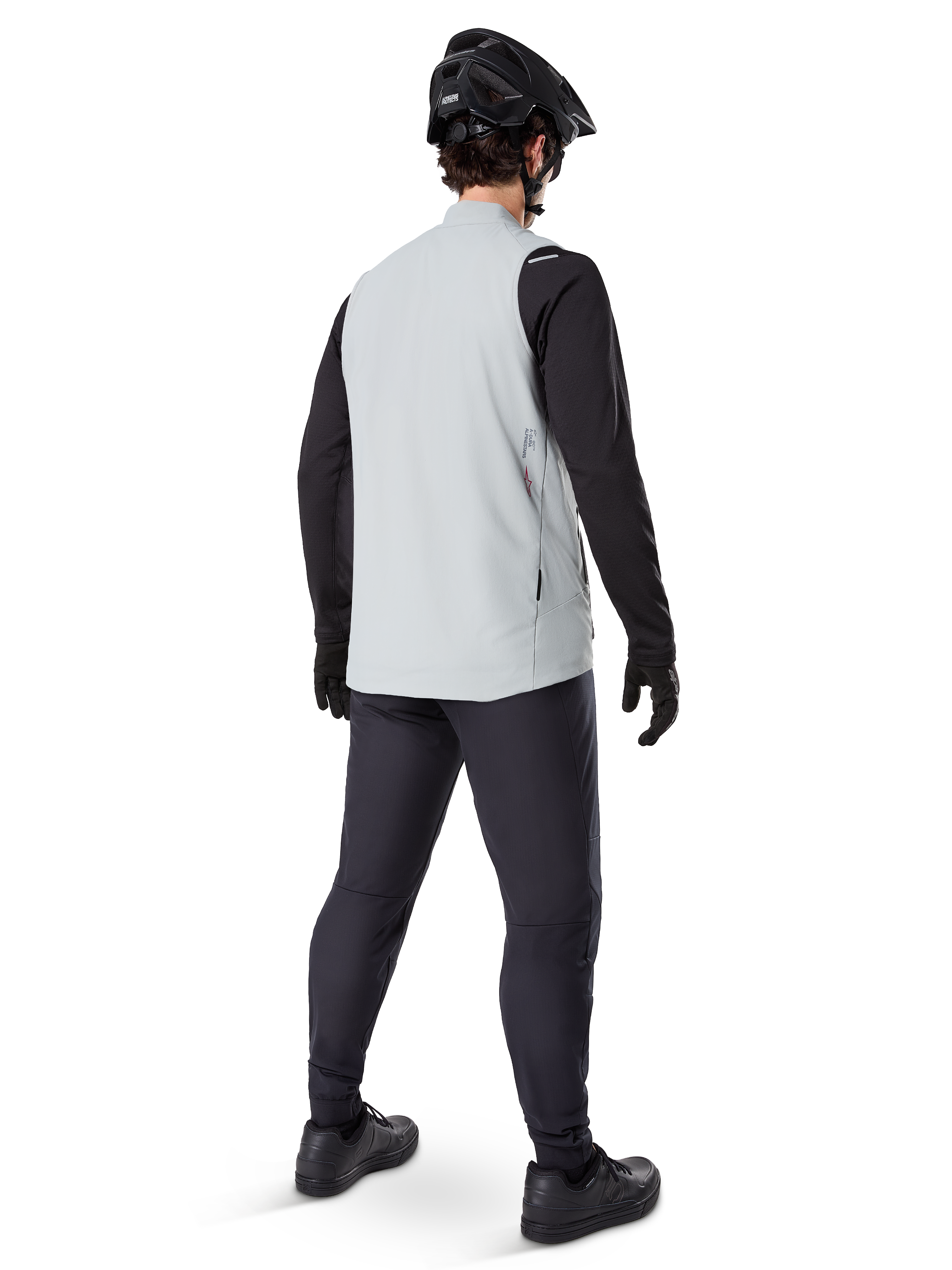 Alpinestars A-Dura Thermovest, Titanium Gray, achteraanzicht van een model dat het geïsoleerde fietsvest draagt over een zwart shirt met lange mouwen en een donkere broek, compleet met zwarte mountainbikehelm en handschoenen, ontworpen voor off-road ritten in koud weer