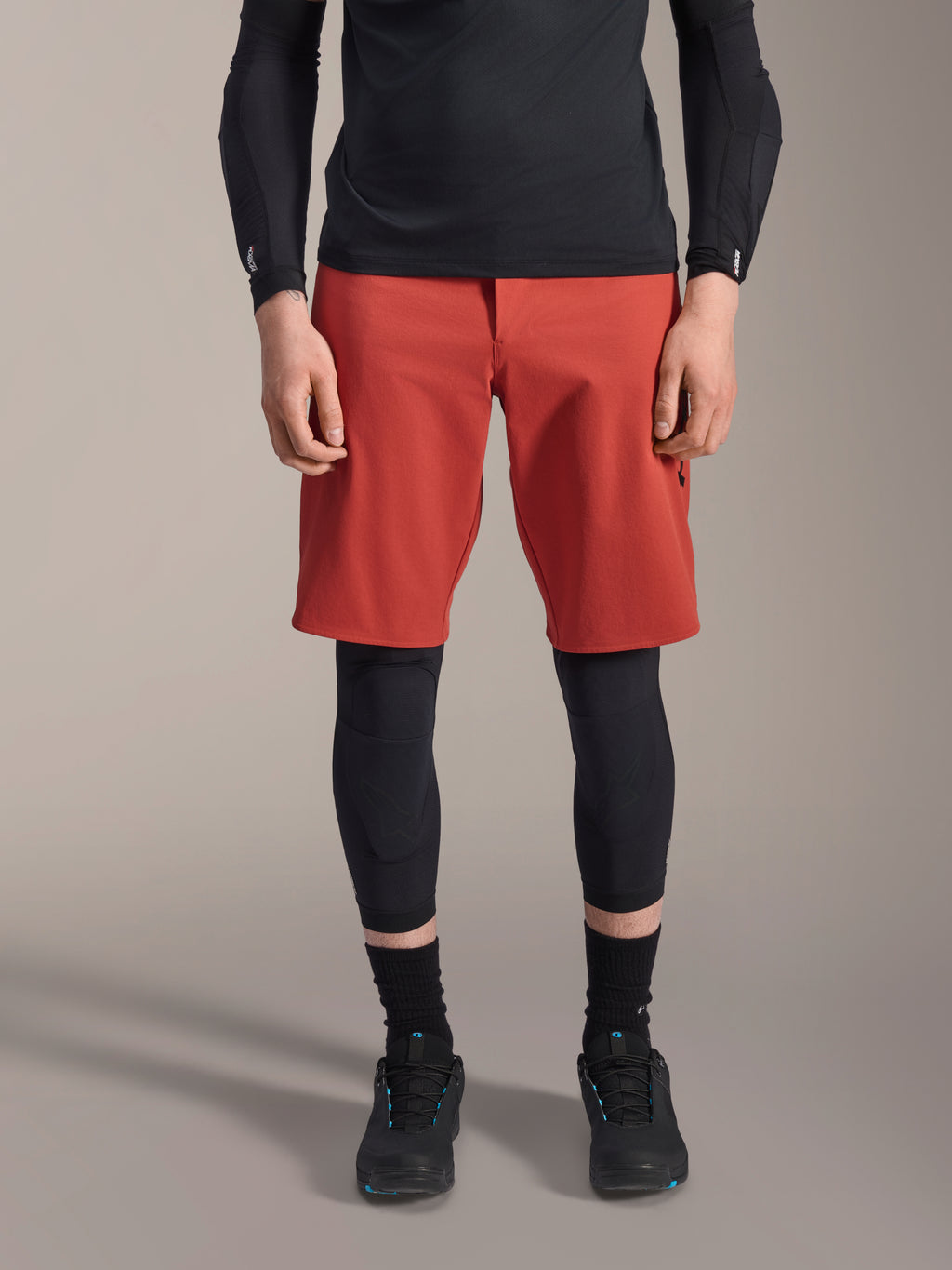 Alpinestars A-Motion Plasma Knee Sleeve, zwarte MTB kniebeschermer, gedragen met rode shorts en zwart shirt met lange mouwen, slank ergonomisch ontwerp, lichtgewicht mesh-constructie voor off-road rijden