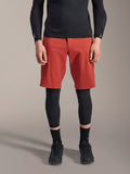 Alpinestars A-Motion Plasma Knee Sleeve, zwarte MTB kniebeschermer, gedragen met rode shorts en zwart shirt met lange mouwen, slank ergonomisch ontwerp, lichtgewicht mesh-constructie voor off-road rijden