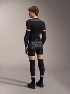Model wearing Alpinestars A-Motion Plasma Protection Boxers in Black Camo and matching A-Motion Plasma Protection Jacket, rear view showing grey camouflage pattern, elbow guards, knee protectors, and cycling shoes, complete mountain bike protection gear setup.