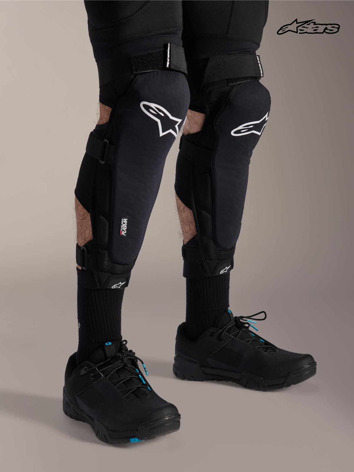 Alpinestars A-Impact Plasma Pro knie-/scheenbeenbeschermers, mountainbike kniebeschermers in zwart met wit logo, gedragen door een model met drievoudig sluitsysteem en Nucleon Plasma bescherming