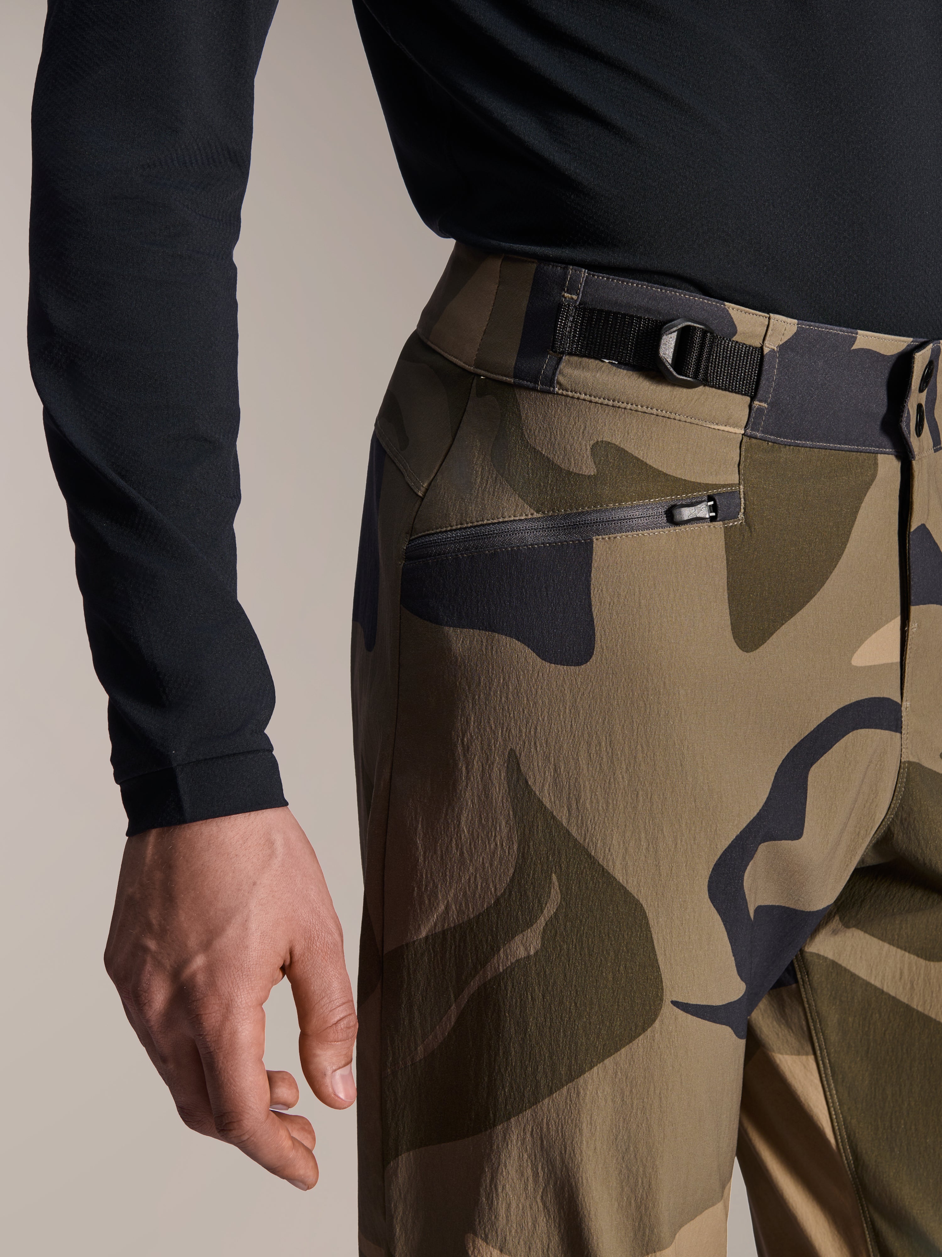 Alpinestars A-Dura Camo broek, MTB-broek, bruine camouflage, close-up van de verstelbare tailleband aan de zijkant en zak met ritssluiting en mesh-voering, duurzame 2-way stretchstof voor mountainbiken