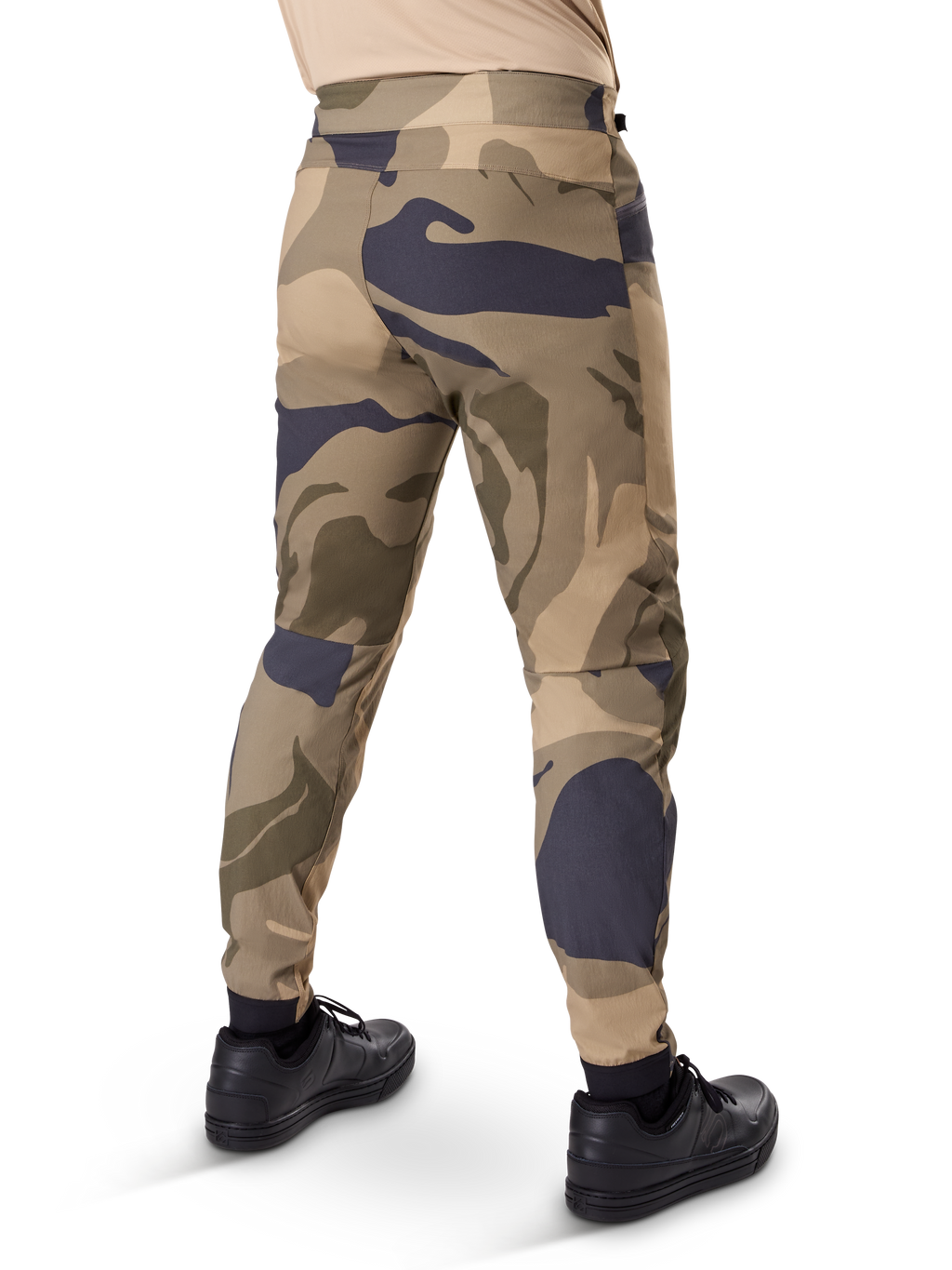 Alpinestars A-Dura Camo broek, MTB-broek, bruin camouflagepatroon met beige en donkergrijze accenten, achteraanzicht getoond met zwarte sneakers, voorzien van taps toelopende pijpen en elastische boorden, duurzame 2-way stretchstof voor mountainbiken
