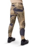 Alpinestars A-Dura Camo broek, MTB-broek, bruin camouflagepatroon met beige en donkergrijze accenten, achteraanzicht getoond met zwarte sneakers, voorzien van taps toelopende pijpen en elastische boorden, duurzame 2-way stretchstof voor mountainbiken