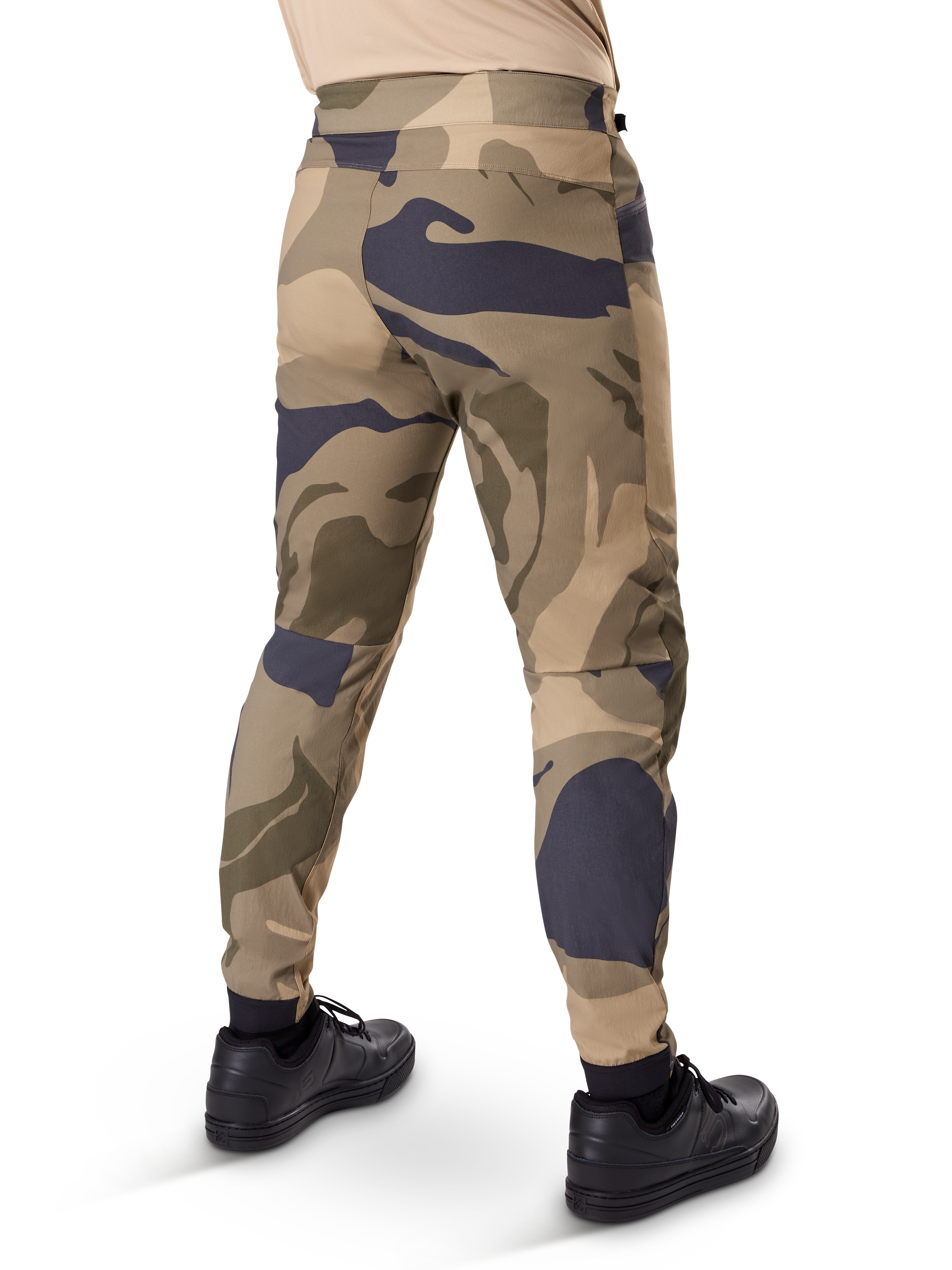 Alpinestars A-Dura Camo broek, MTB-broek, bruin camouflagepatroon met beige en donkergrijze accenten, achteraanzicht getoond met zwarte sneakers, voorzien van taps toelopende pijpen en elastische boorden, duurzame 2-way stretchstof voor mountainbiken