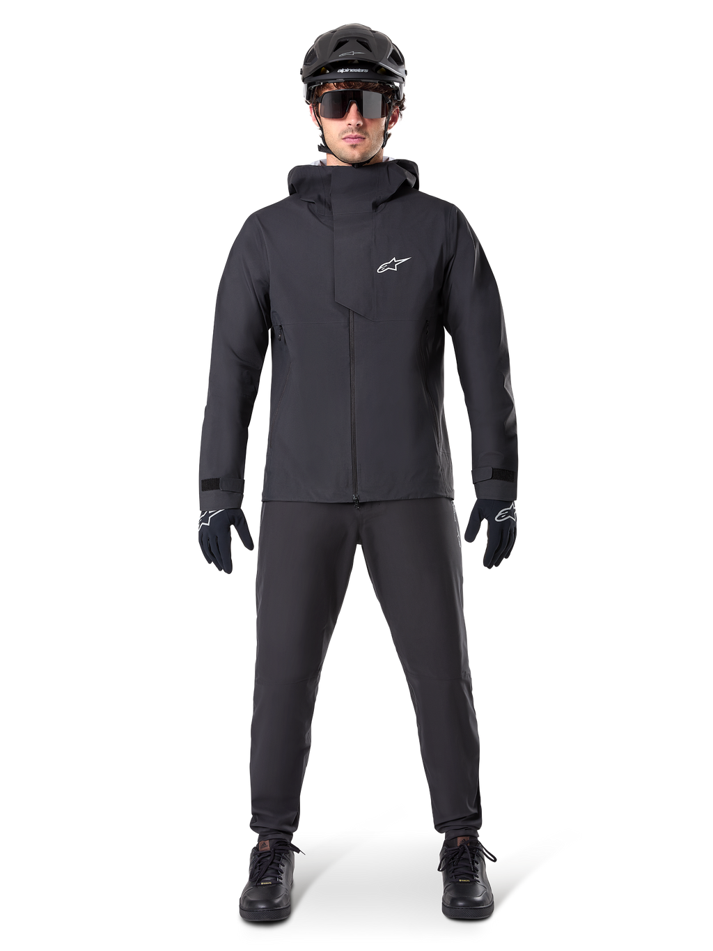 Alpinestars A-Dura Waterproof Pants, zwarte MTB-broek, gedragen als onderdeel van een complete volledig zwarte mountainbike-uitrusting inclusief een technisch waterdicht jack, zwarte helm, zonnebril en handschoenen, ontworpen voor off-road ritten in natte weersomstandigheden.