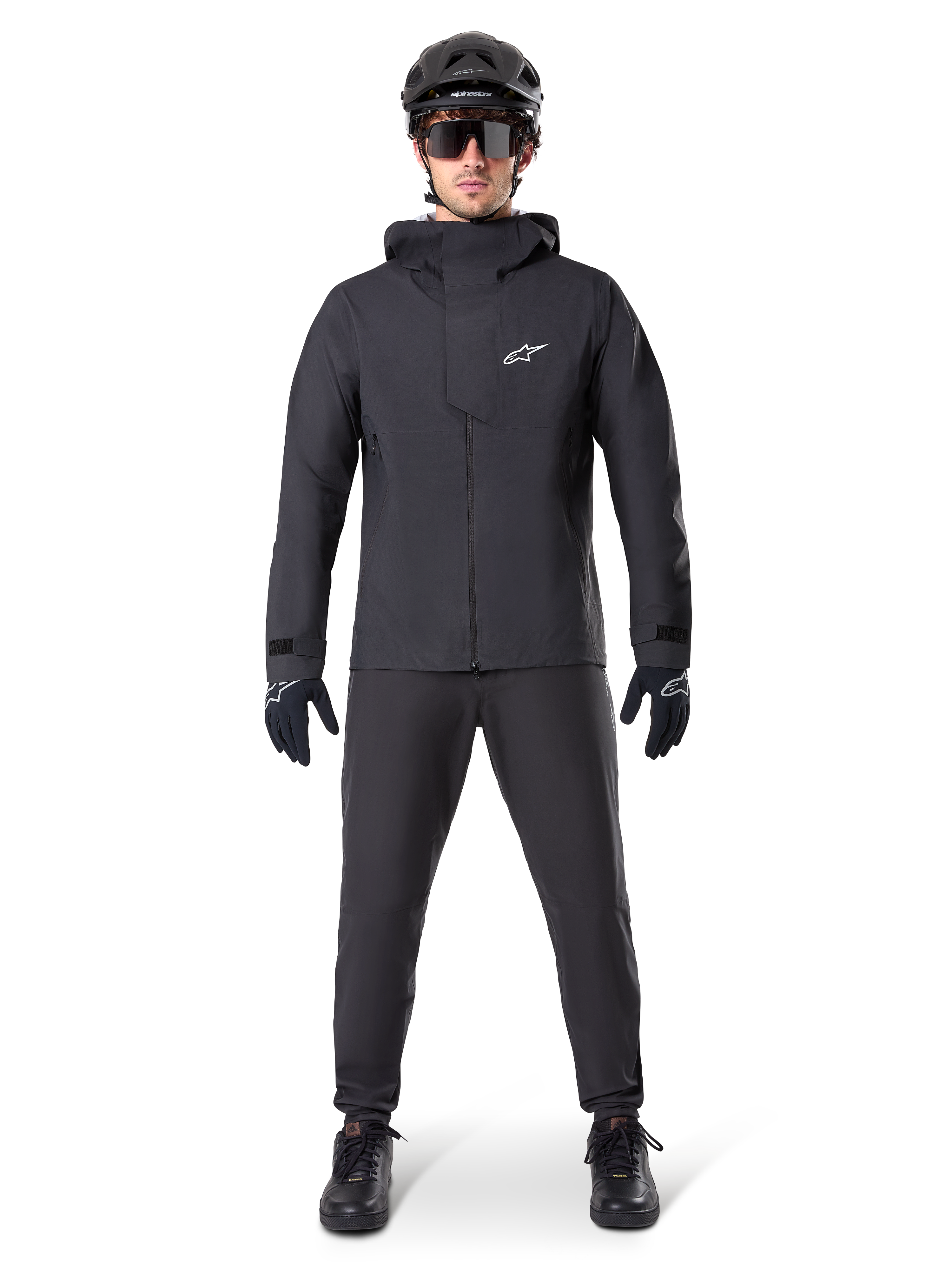 Alpinestars A-Dura Waterproof Pants, zwarte MTB-broek, gedragen als onderdeel van een complete volledig zwarte mountainbike-uitrusting inclusief een technisch waterdicht jack, zwarte helm, zonnebril en handschoenen, ontworpen voor off-road ritten in natte weersomstandigheden.