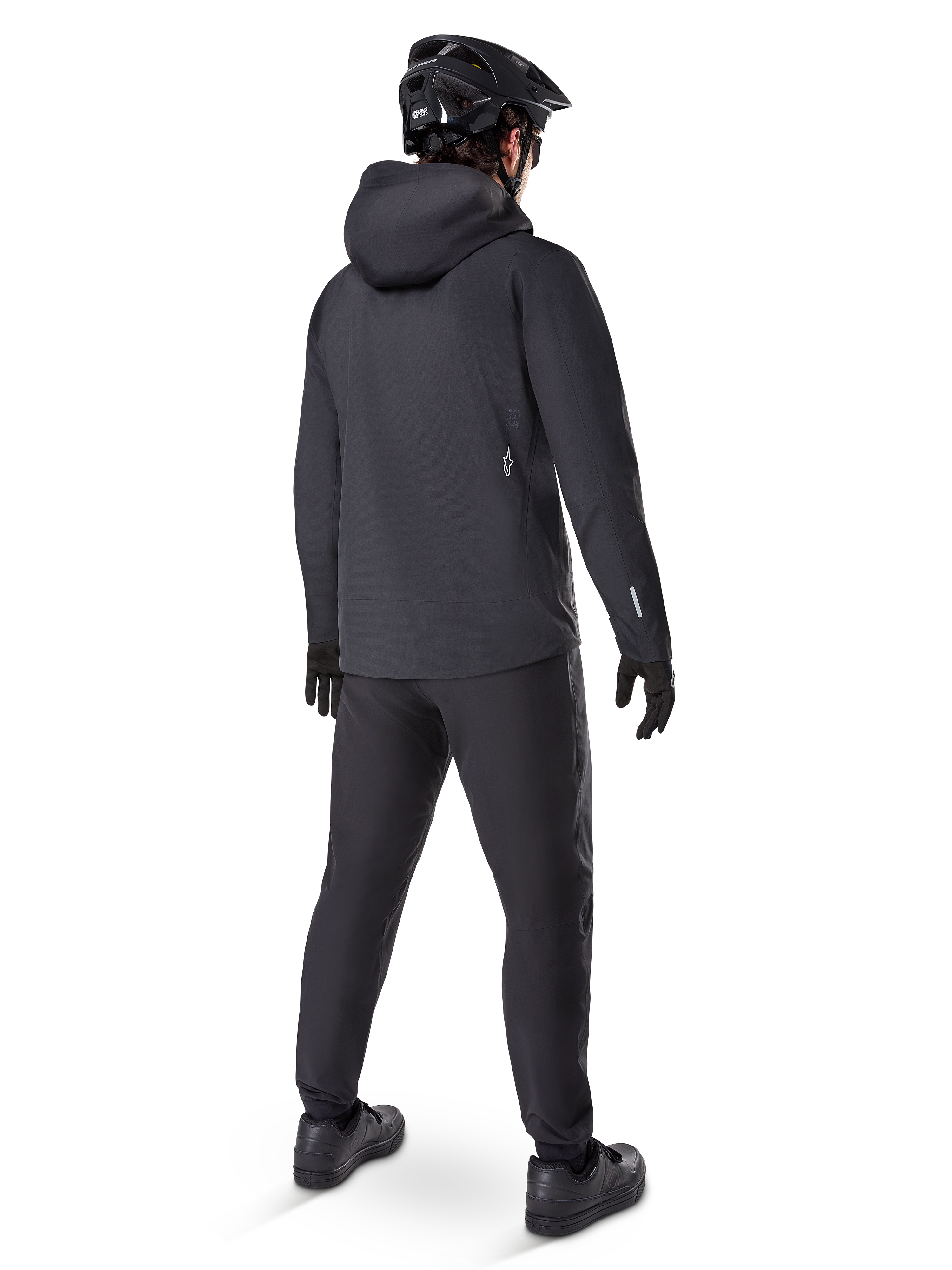 Alpinestars A-Dura Waterdichte Broek, MTB-broek, zwart, van achteren gezien op een rijder in een volledige zwarte mountainbike-outfit inclusief een jas met capuchon en helm, duurzame waterdichte uitrusting voor modderige paden