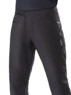 Alpinestars A-Dura Waterproof Pants, mountainbikebroek, zwart, close-up van de taille met ratelsluiting en zakken met rits, met een wit Alpinestars-logo op de dij, duurzaam textiel voor trailrijden in natte weersomstandigheden